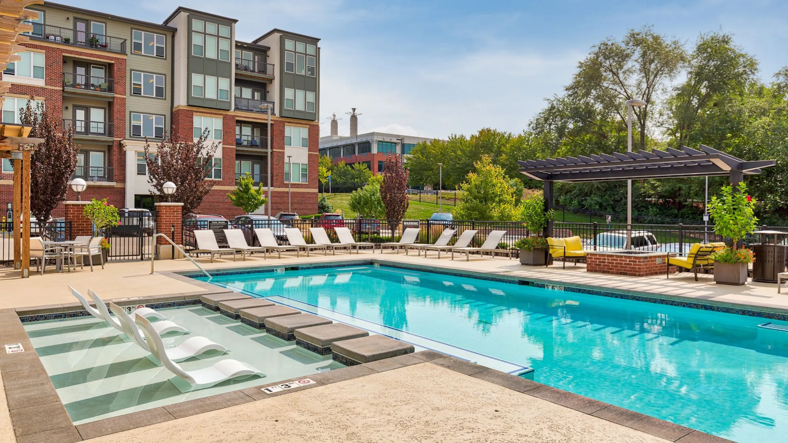 Inviting apartment complex showcasing a pristine swimming pool, stylish poolside lounge chairs, and a charming pergola with vibrant greenery.