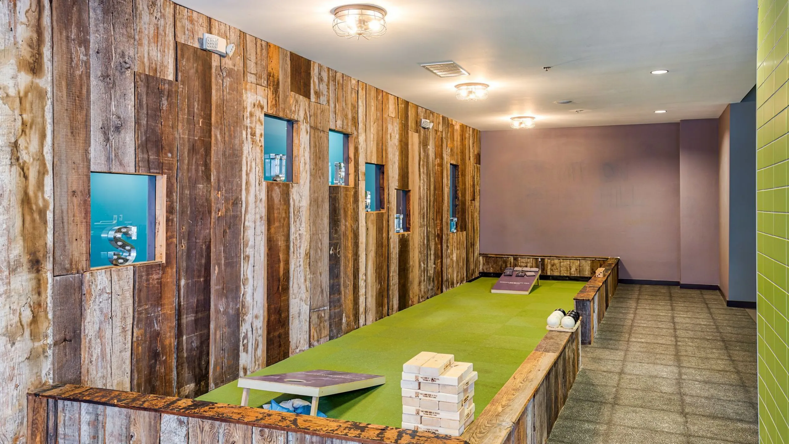 Charming indoor recreation area featuring rustic wood paneling and a green carpeted surface, perfect for casual games and social gatherings.