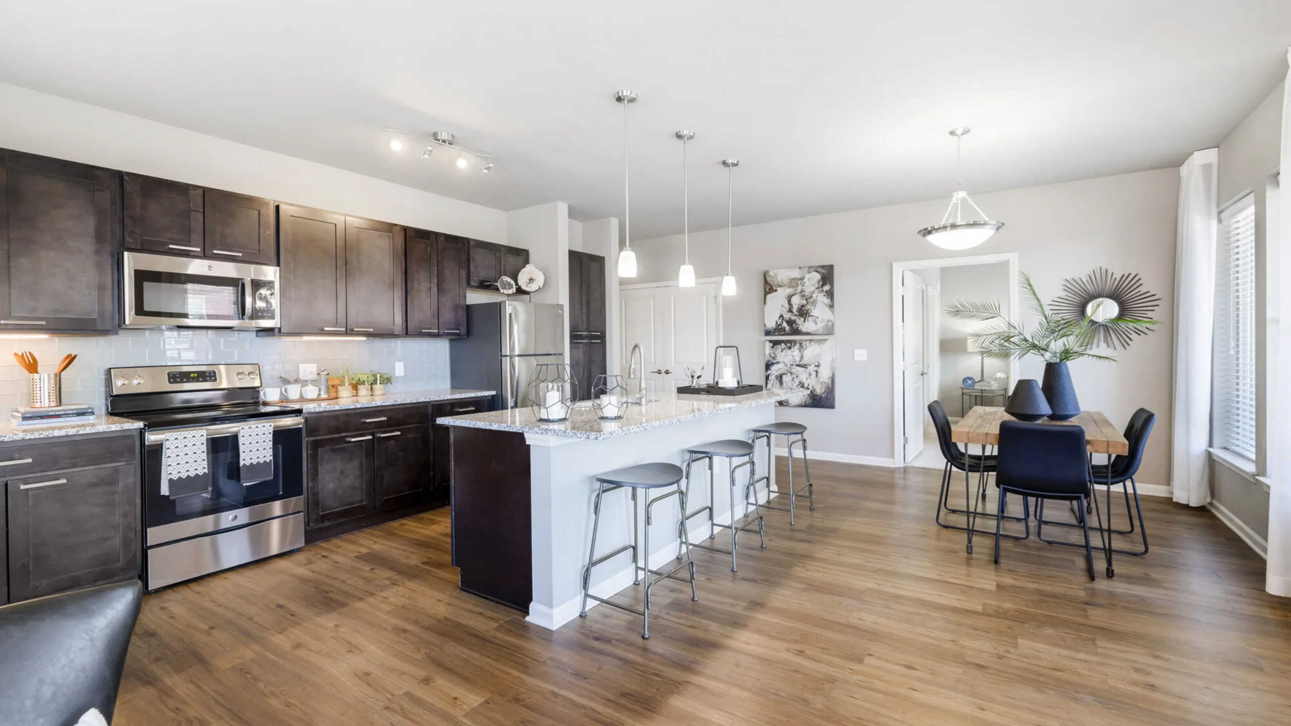 Modern open-concept kitchen and dining area with sleek dark cabinetry, stainless steel appliances, and a stylish wooden dining table set.