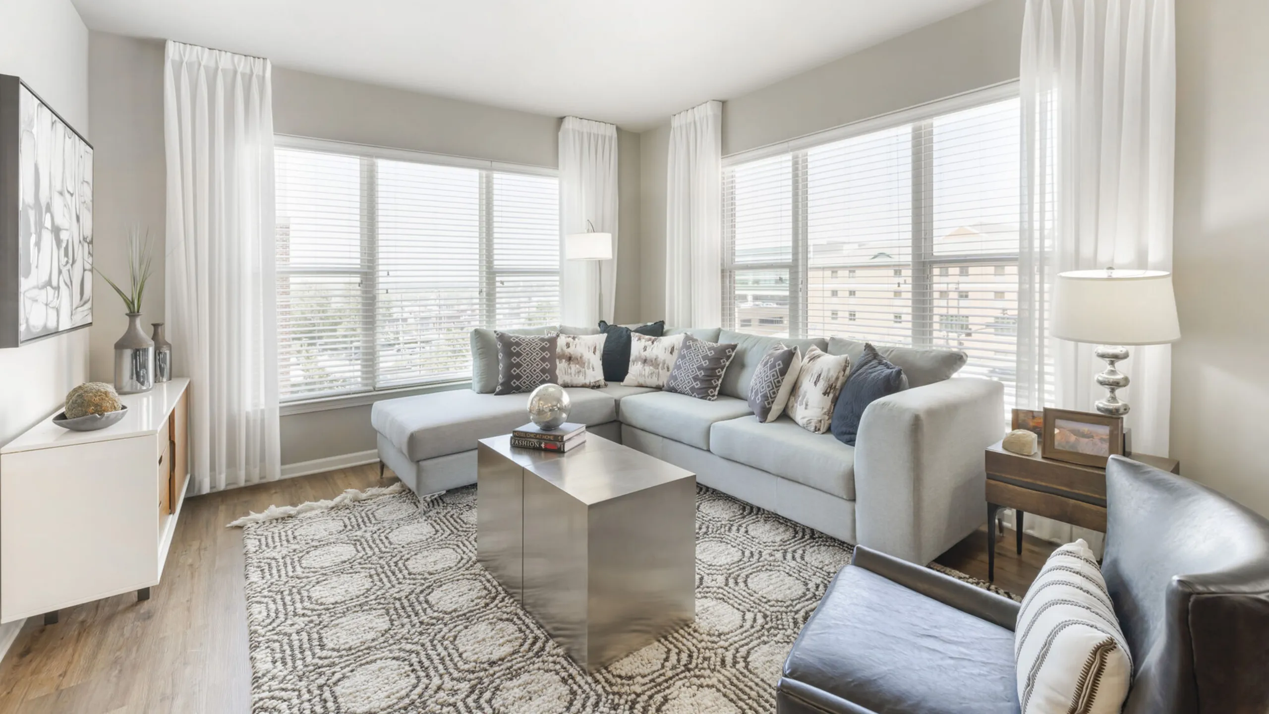 Bright and elegant living room with large windows, modern sectional sofa, chic decor, and a stylish area rug.