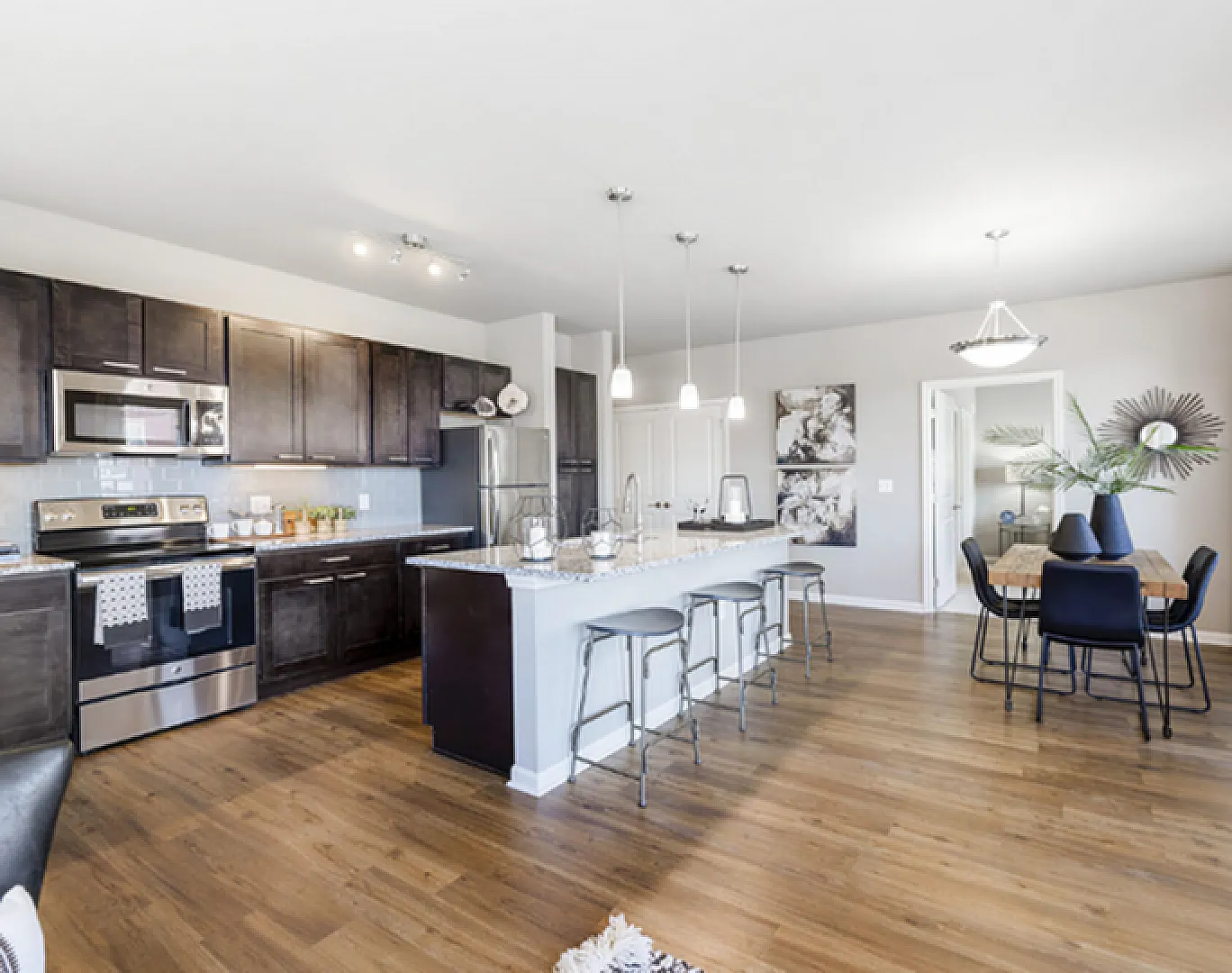 Modern open-concept kitchen with sleek dark cabinetry, elegant island seating, stainless steel appliances, and a cozy dining area on wooden flooring.