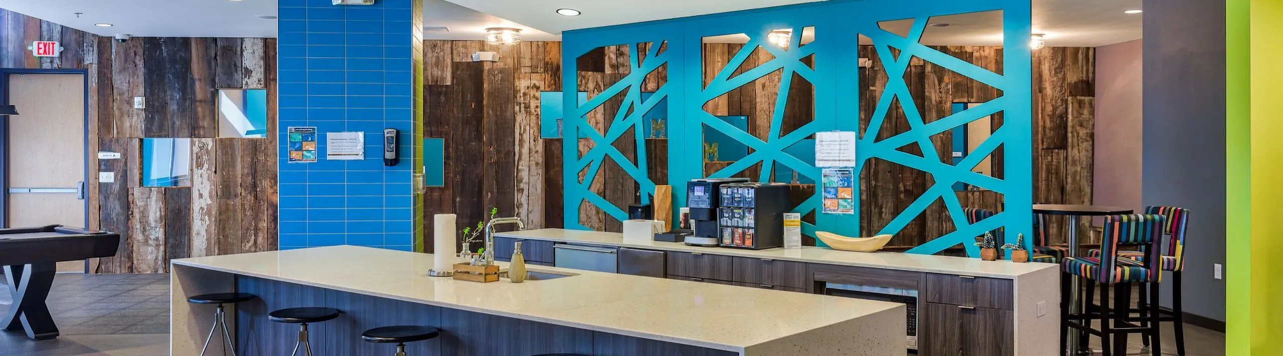 Modern communal kitchen with chic decor, featuring vibrant blue accents, stylish seating, and a sleek island countertop.