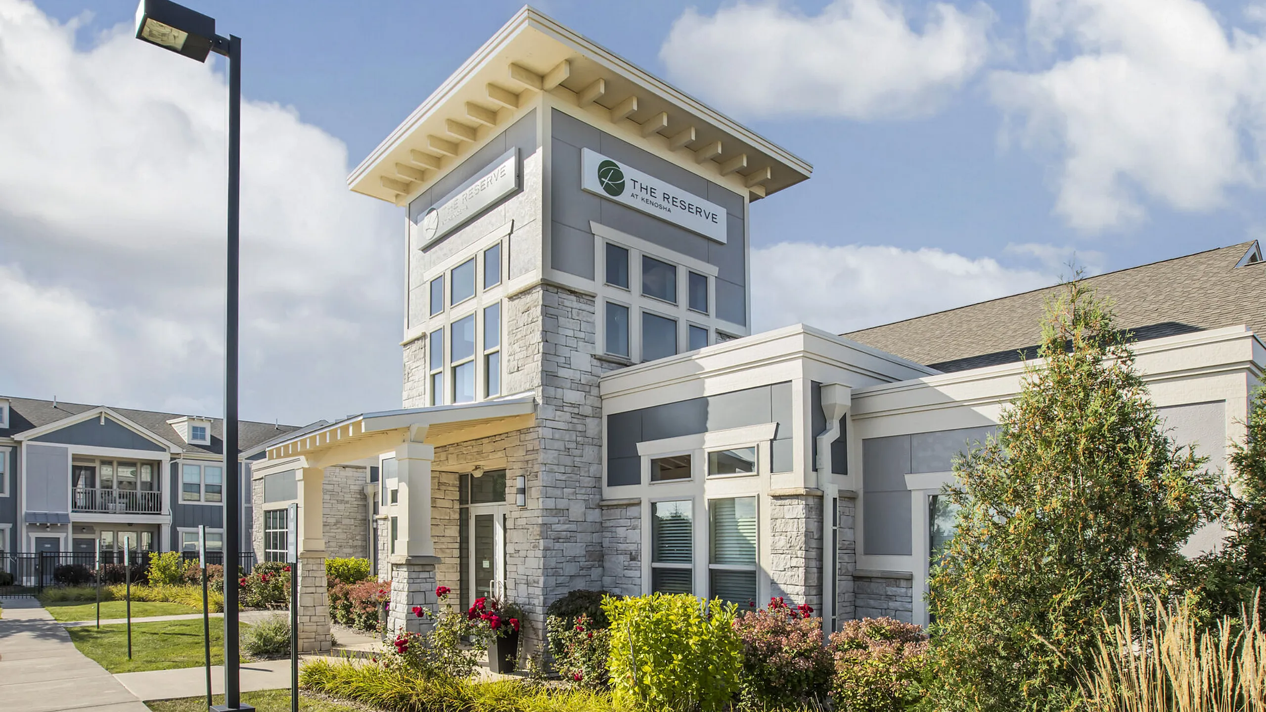 Chic apartment complex exterior with modern stone and glass architecture, lush landscaping, and inviting entrance.
