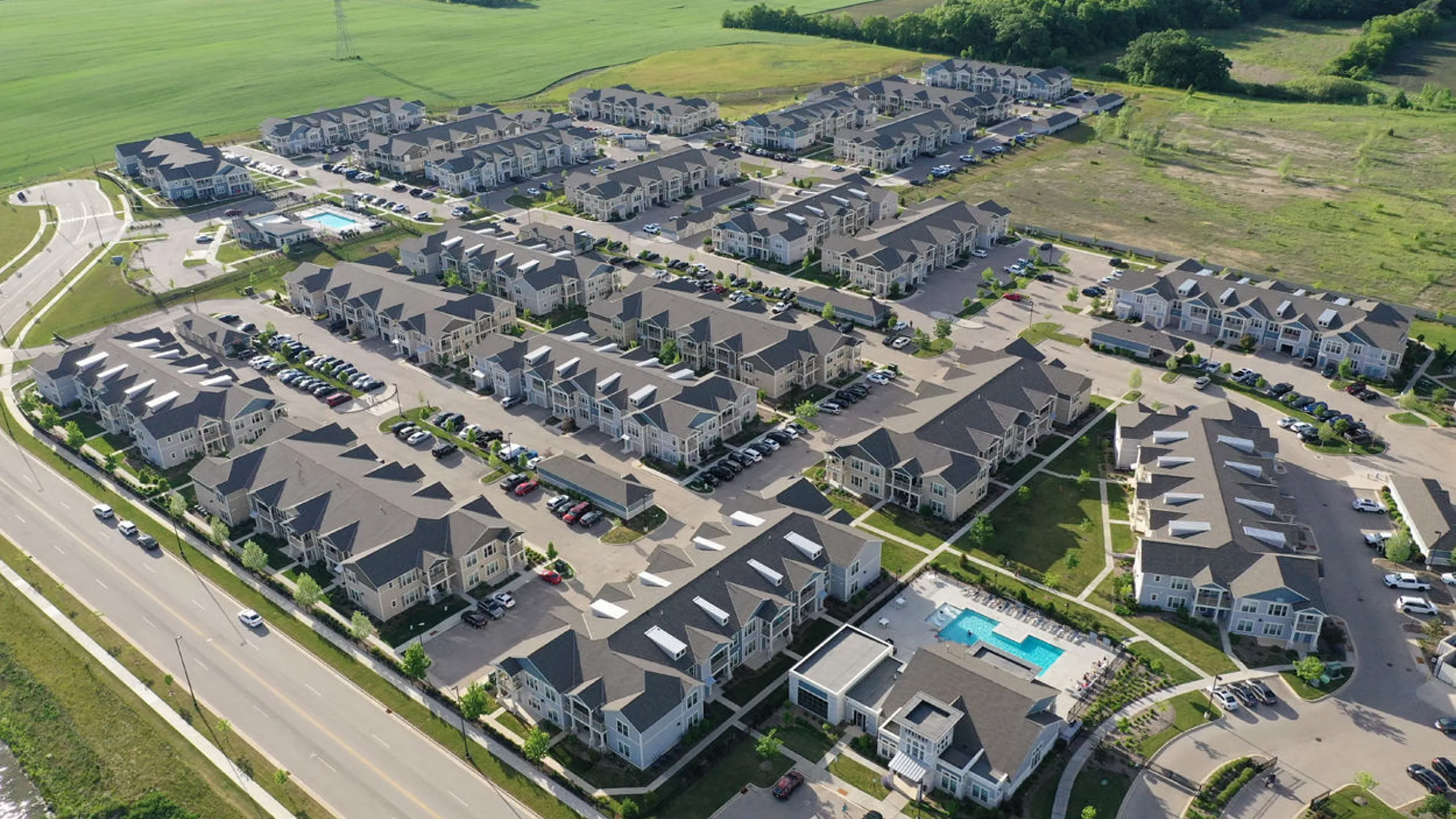 Stunning aerial view of a modern apartment complex with beautifully landscaped grounds, ample parking, and inviting swimming pools, set amidst lush greenery.