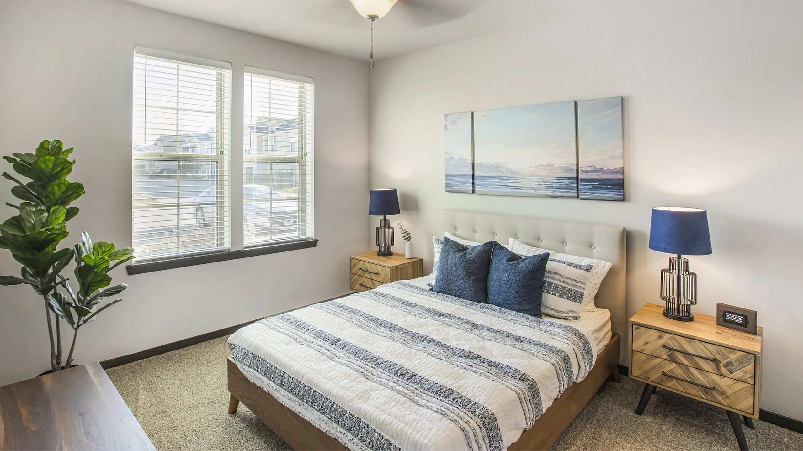 Bright and inviting bedroom with modern decor, featuring a cozy bed with patterned bedding, dual nightstands with stylish lamps, and large windows allowing natural light to flood the space.