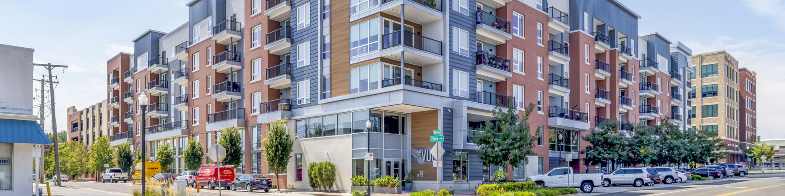 Contemporary apartment complex with modern architecture, surrounded by lush greenery and ample parking spaces.