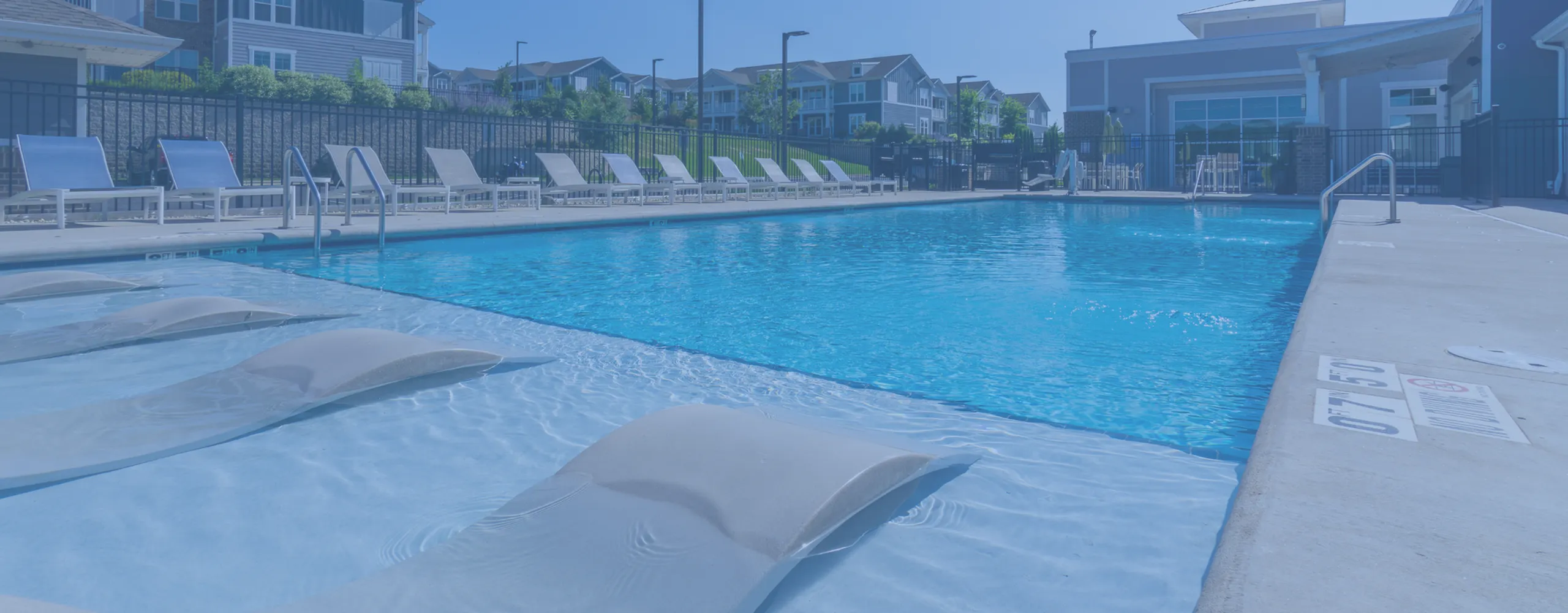 Inviting outdoor pool area with comfortable lounge chairs and blue umbrellas, perfect for relaxation and enjoying sunny days.