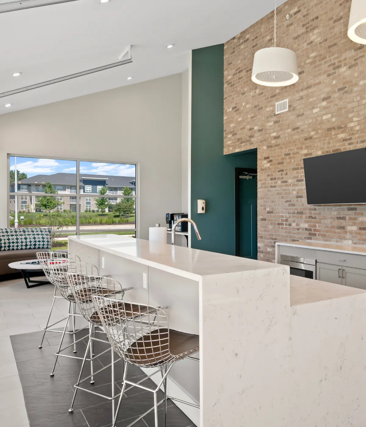 Modern apartment clubhouse featuring elegant open kitchen with sleek cabinetry, cozy seating area, and contemporary lighting design.