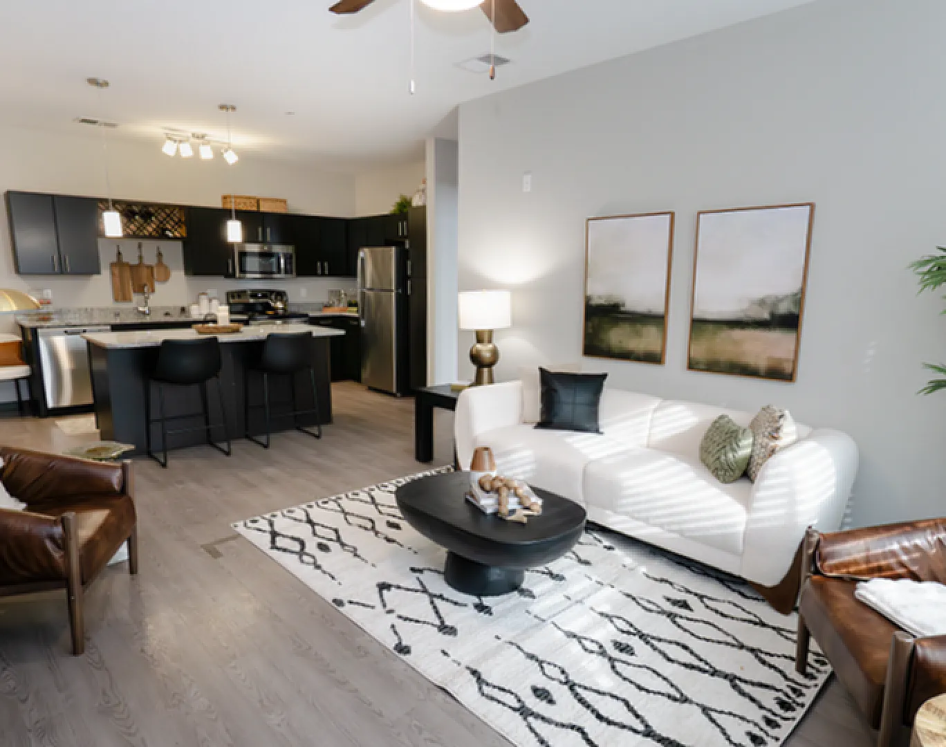 Modern open-concept living room with stylish decor, featuring a sleek kitchen, comfortable seating, and chic artwork.