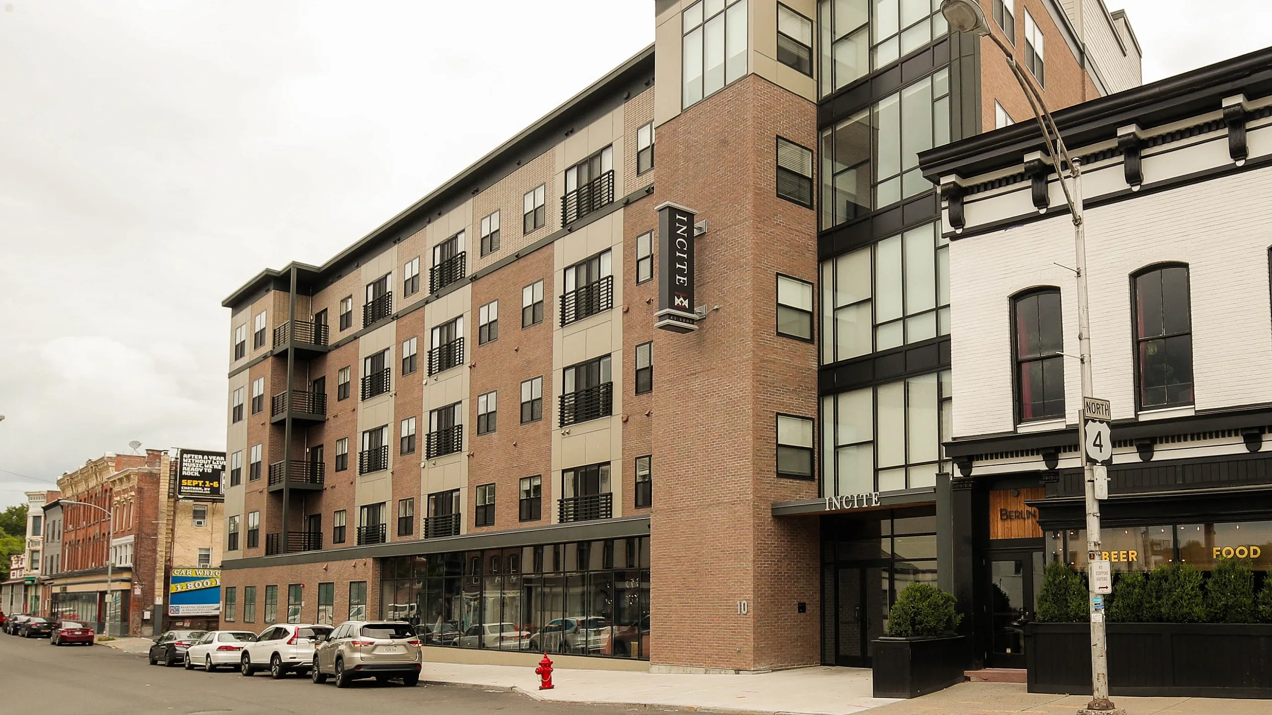 Modern residential building with sleek design and expansive windows above a bustling street corner, featuring a vibrant restaurant below.