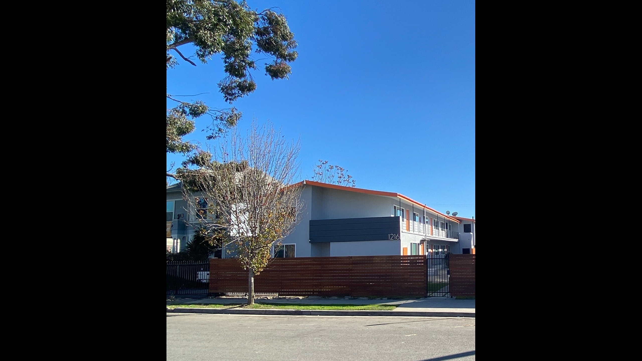 Modern two-story apartment building with sleek architecture, large windows, and a spacious outdoor area, set against a clear blue sky.