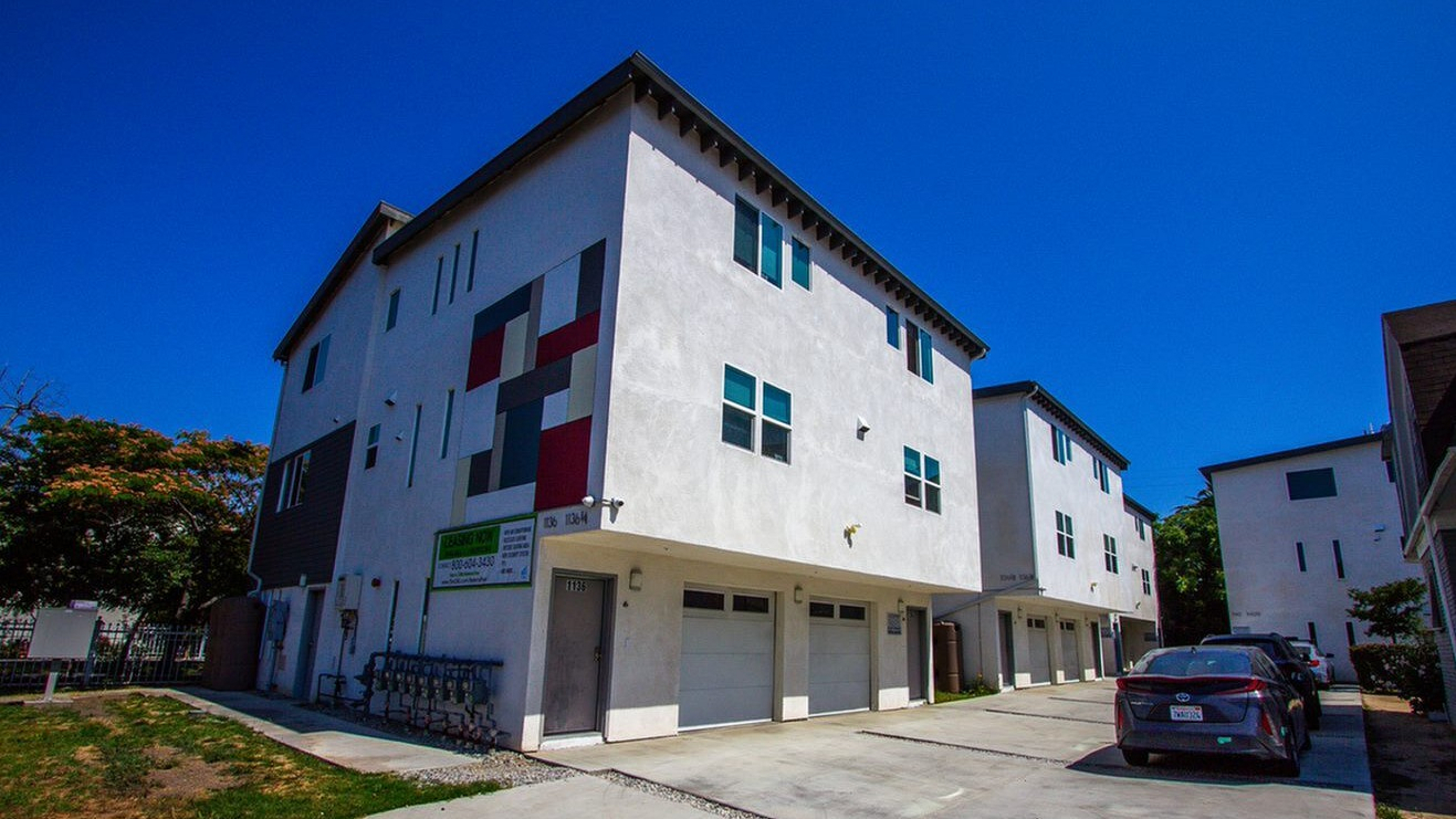 Modern townhouse complex with bold geometric exterior design, offering ample parking and a sunlit setting.