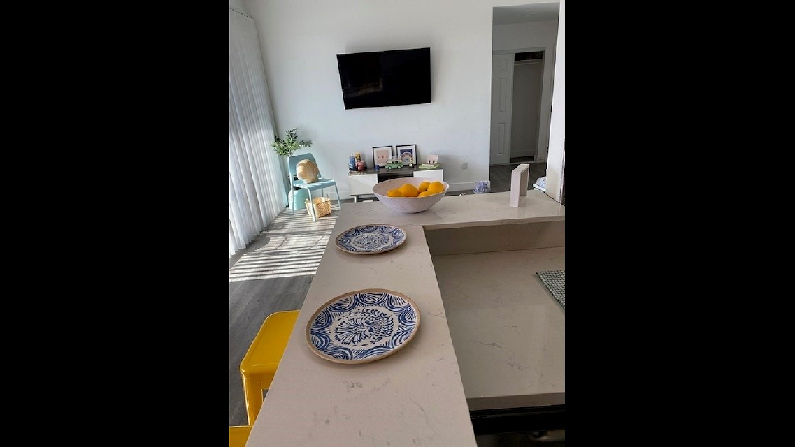 Bright and modern kitchen with sleek countertops, decorative blue plates, and a vibrant living area with a mounted TV and stylish decor.