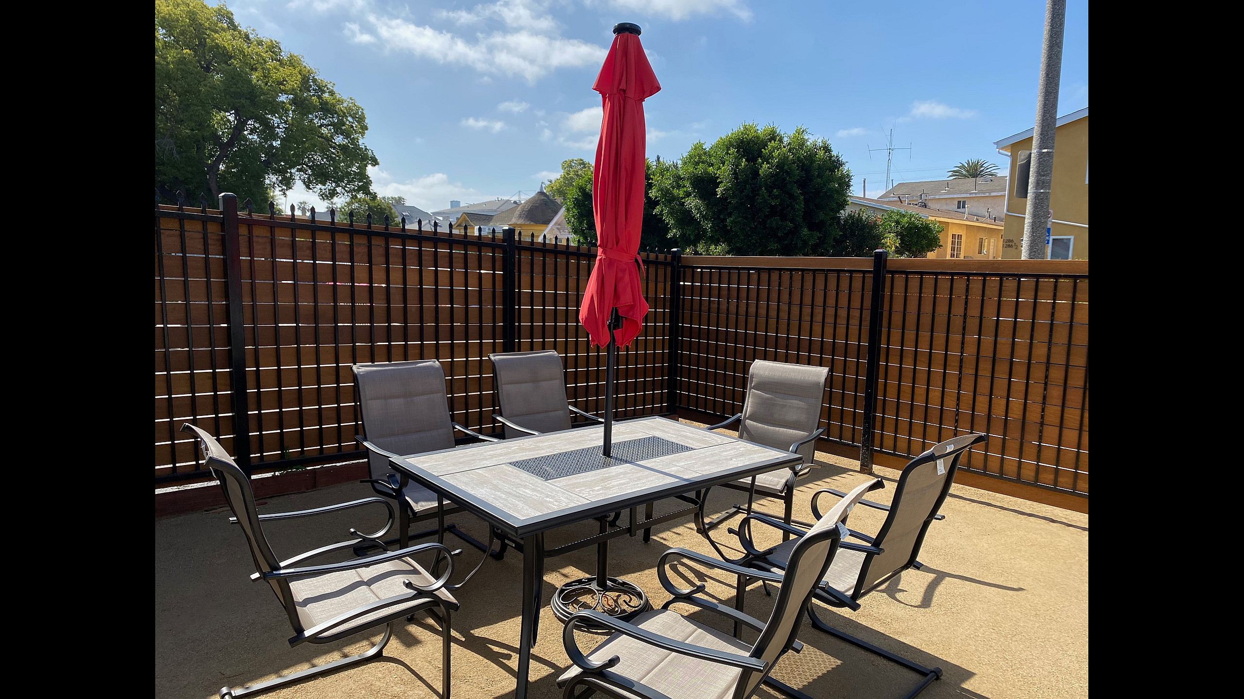 Inviting outdoor patio with six chairs and a stylish table featuring a vibrant red umbrella, perfect for entertaining guests under clear blue skies.
