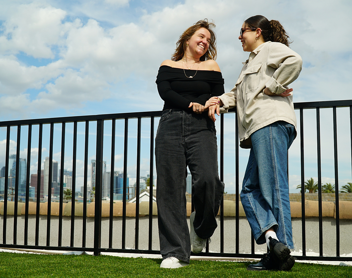 Two friends enjoying a sunny day on a spacious rooftop terrace, with a scenic city skyline in the background.
