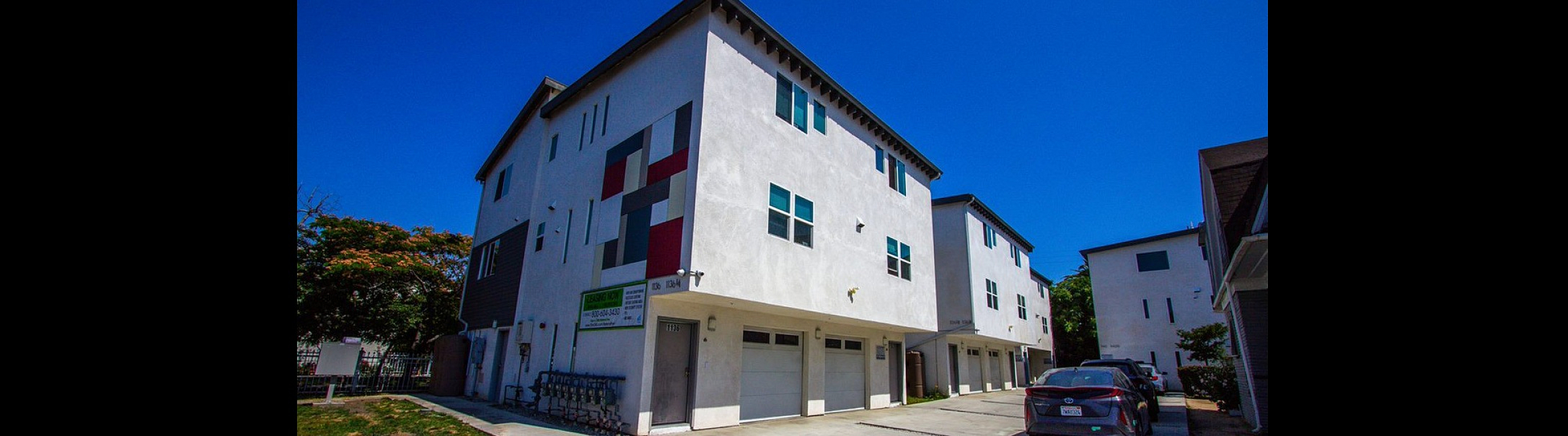 Modern townhouse complex with distinctive geometric design, featuring a bright facade and multiple garage spaces under a clear blue sky.