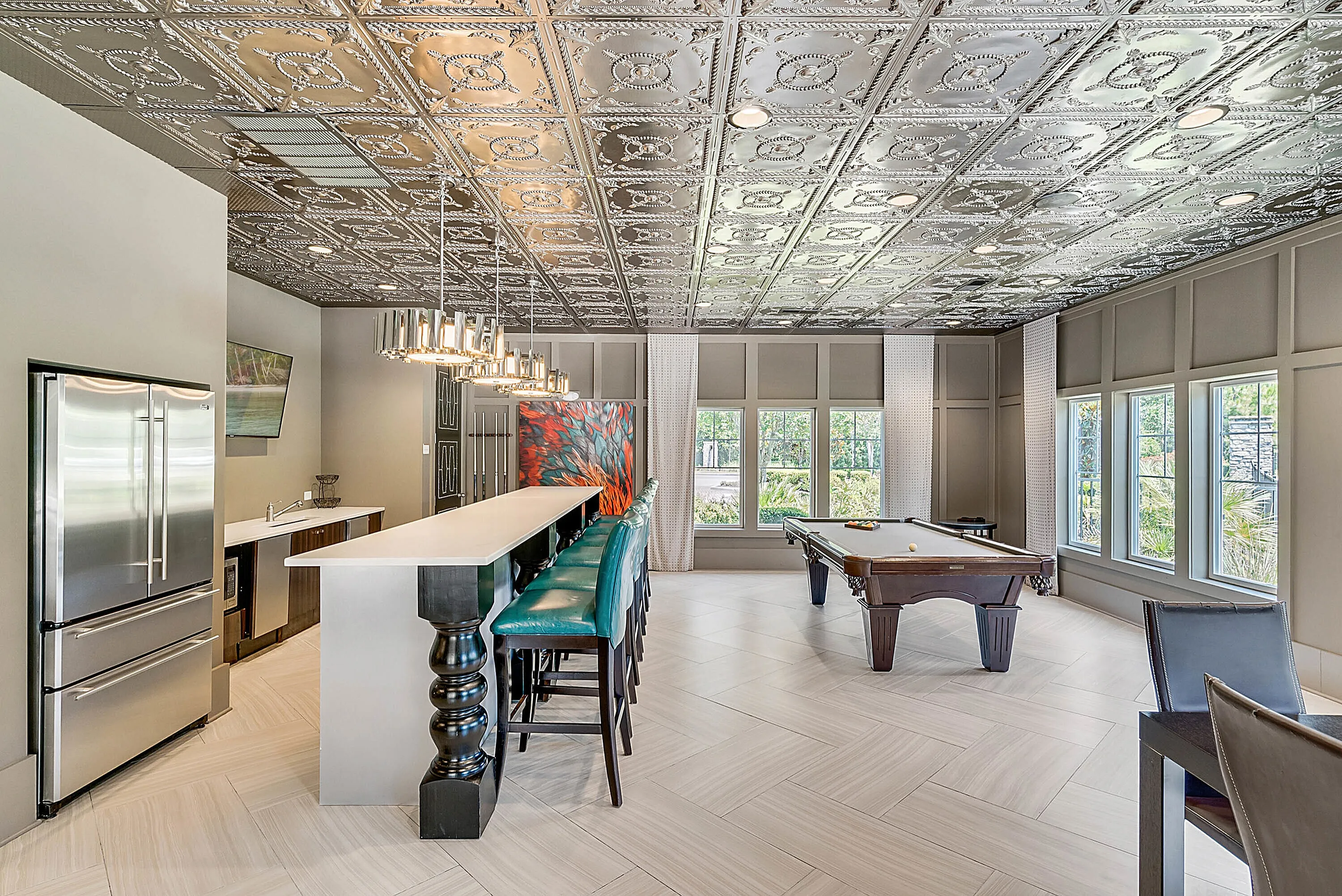 Luxurious entertainment room featuring a sleek bar with modern stools, elegant tin ceiling, and a stylish pool table with scenic window views.