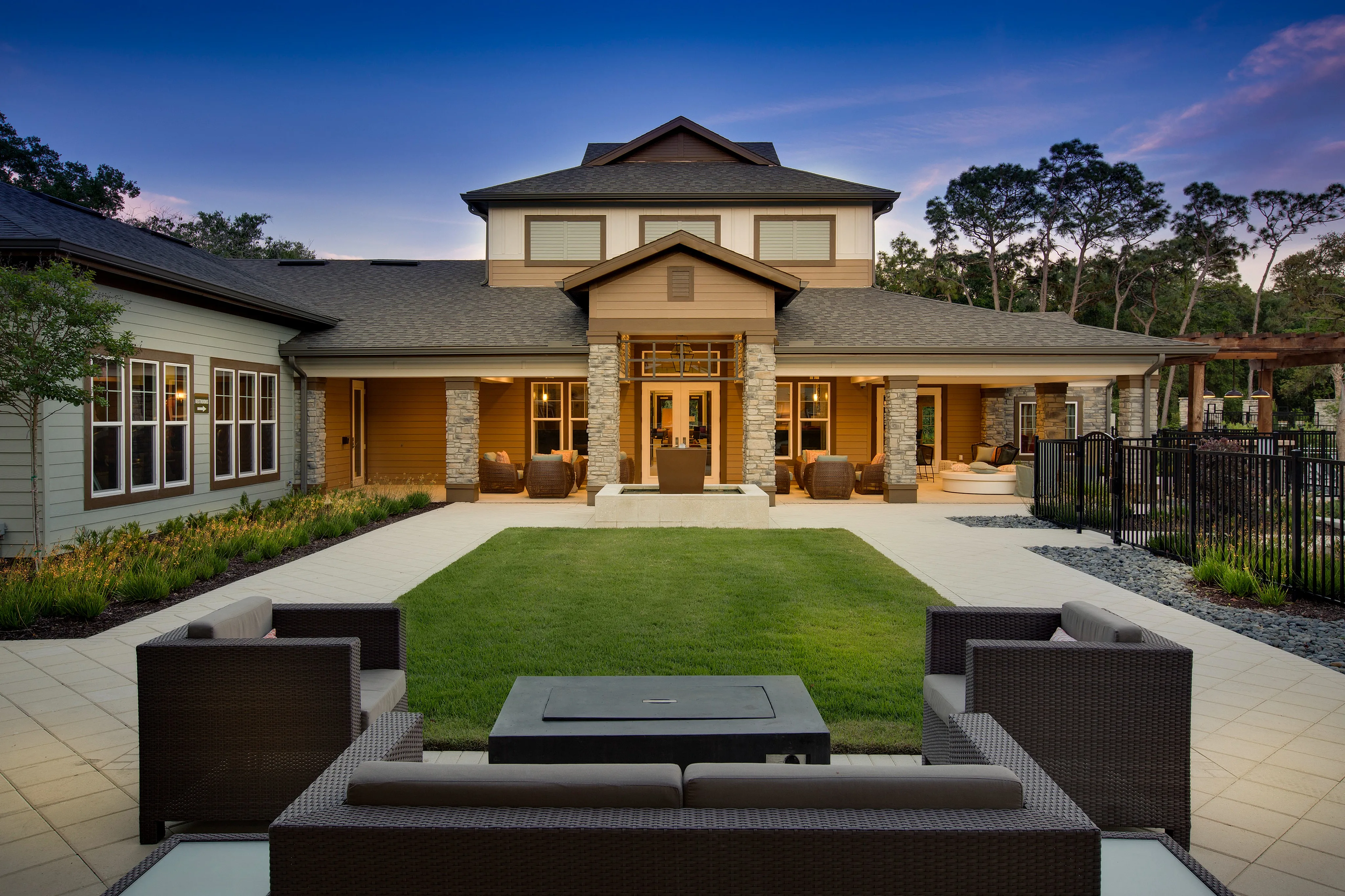 Luxurious two-story residence with inviting stone accents, beautifully landscaped courtyard, and elegant outdoor seating area under a serene evening sky.