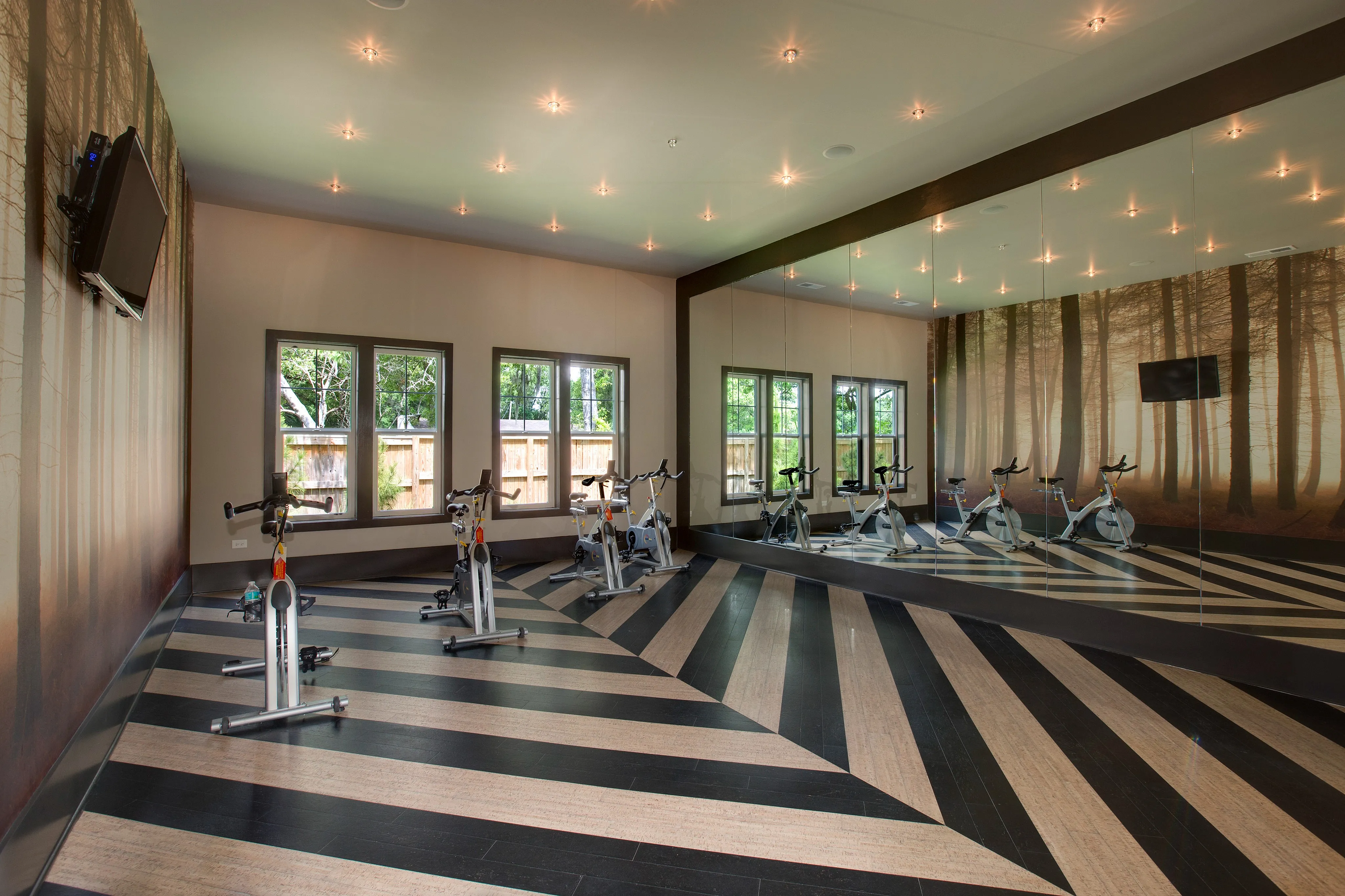 Chic indoor cycling room featuring sleek spin bikes, mirrored walls, and expansive windows with forest-themed decor.