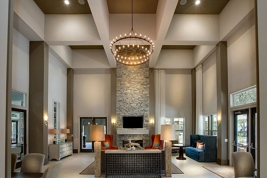 Luxurious high-ceiling lounge with elegant stone fireplace, chic chandelier, and modern seating in a refined apartment setting.