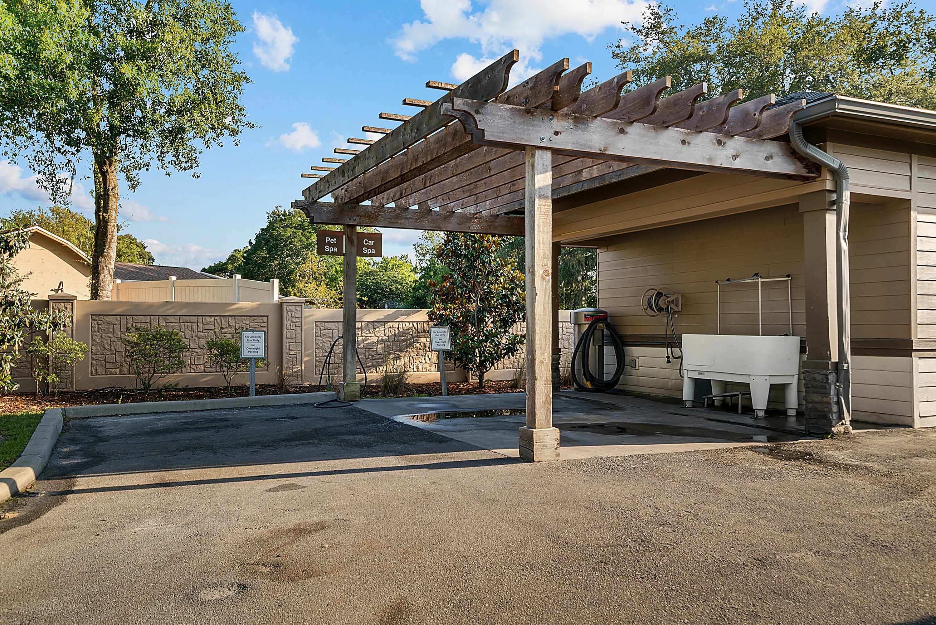 Charming outdoor pet and car spa area with a rustic wooden pergola set against a landscaped background.