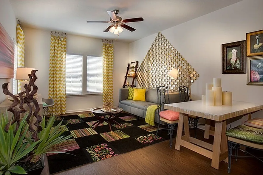 Chic living room with vibrant decor, featuring a cozy gray sofa, geometric wall art, and colorful patterned rug, accented by warm lighting and stylish furnishings.