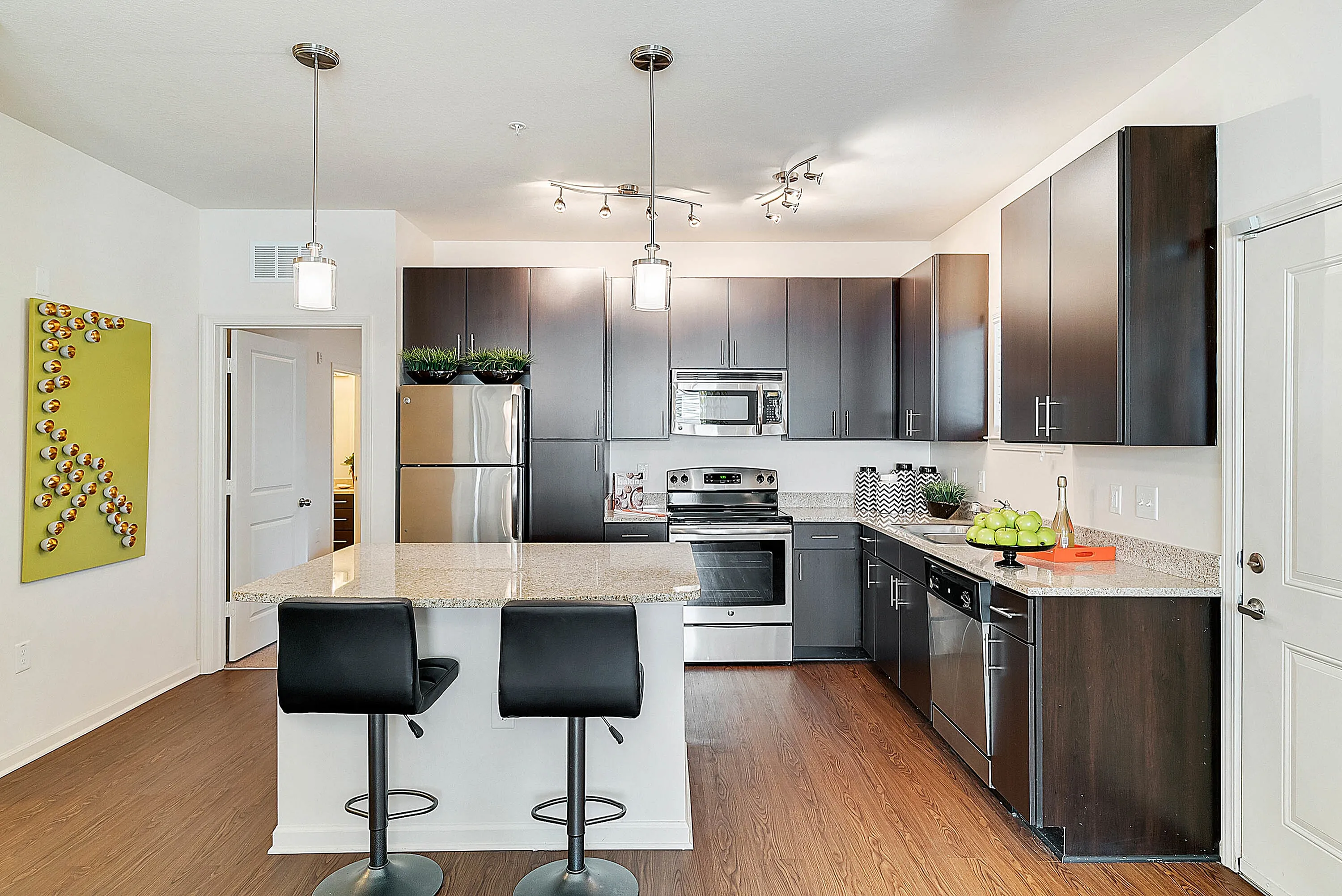Contemporary kitchen with sleek dark wood cabinets, granite countertops, and modern appliances, complemented by elegant pendant lighting and stylish bar stools.