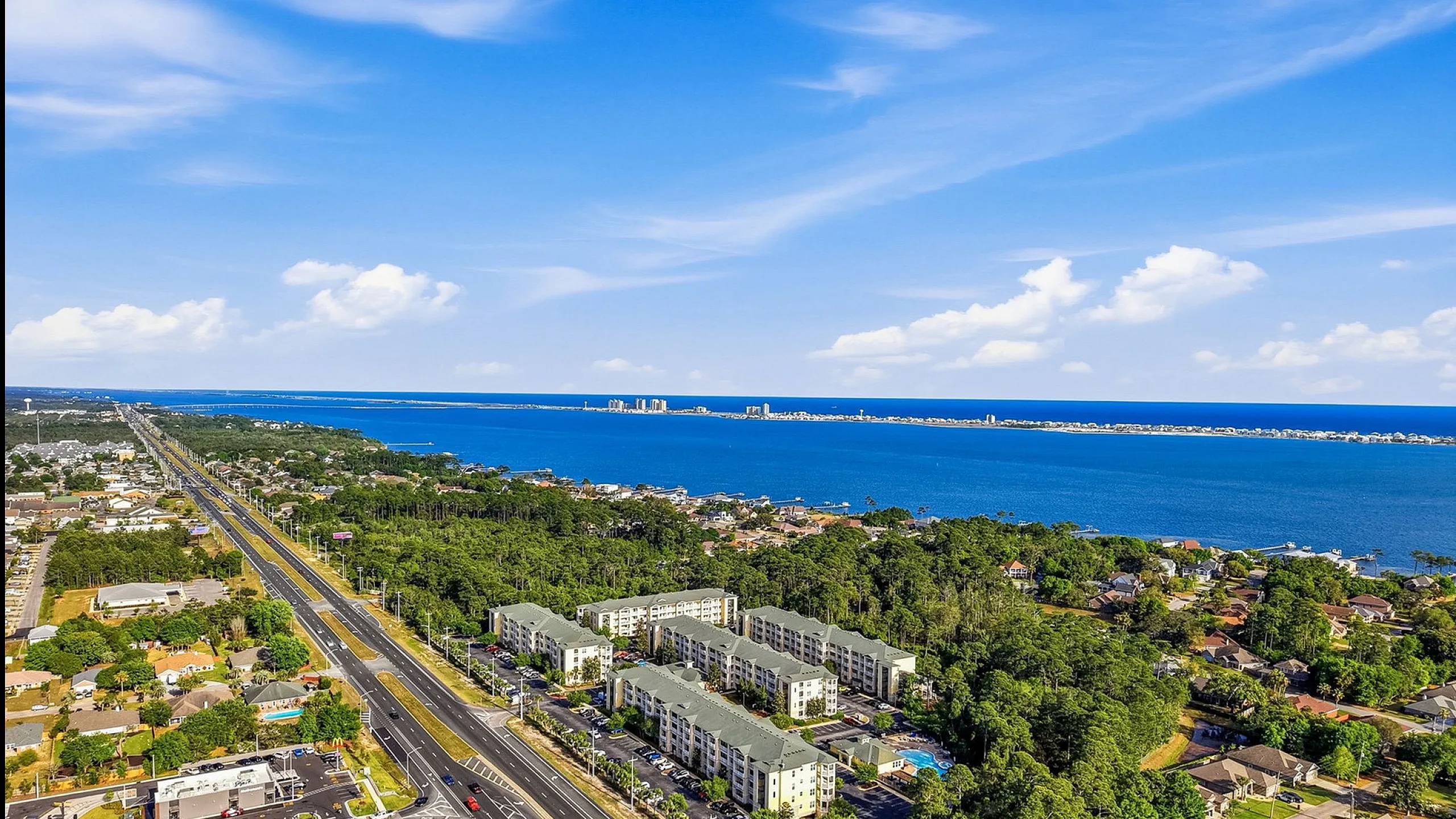 Breathtaking aerial view of a vibrant coastal community with lush greenery, modern apartments, and serene waterfront panorama.