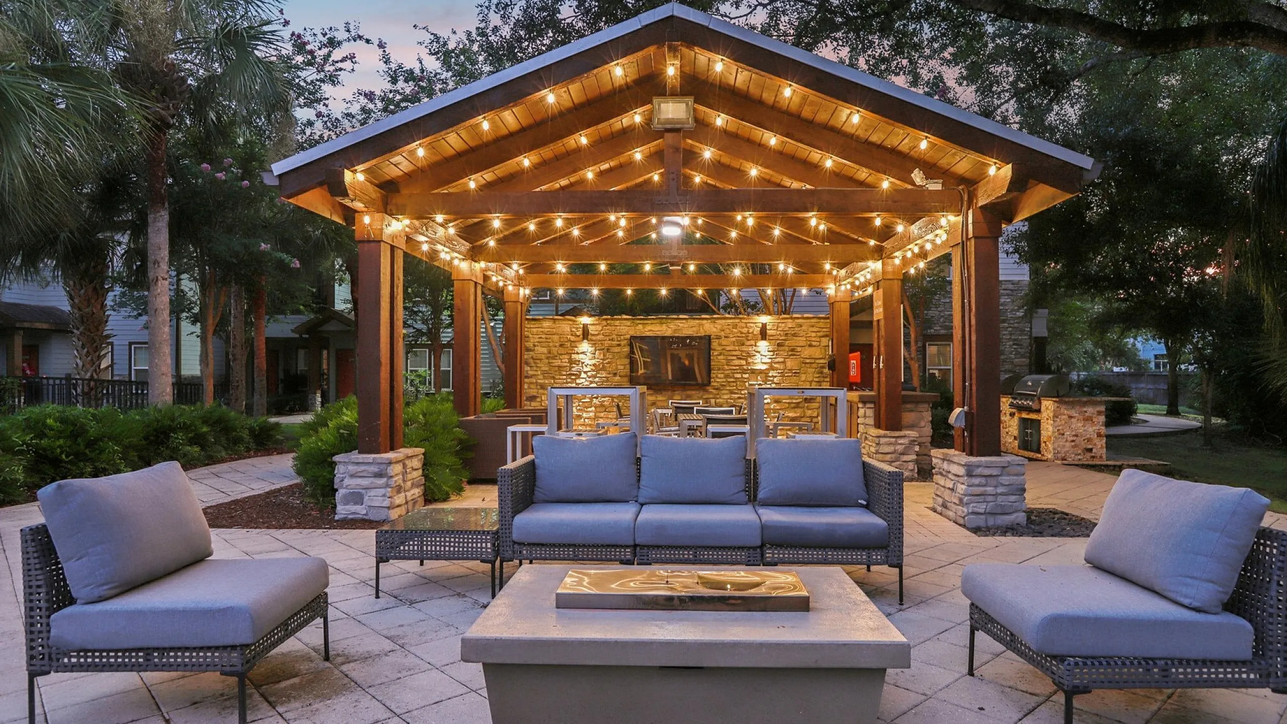 Charming outdoor patio featuring cozy wicker seating, a modern fire pit, and a pergola adorned with string lights, perfect for evening relaxation.