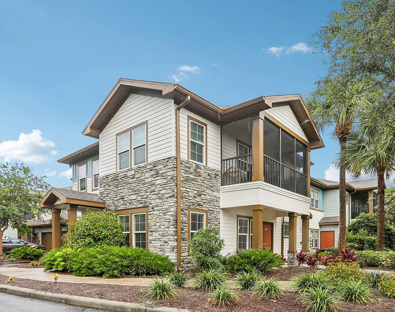Charming two-story house with stone accents and lush landscaping, featuring a spacious screened porch and elegant design.
