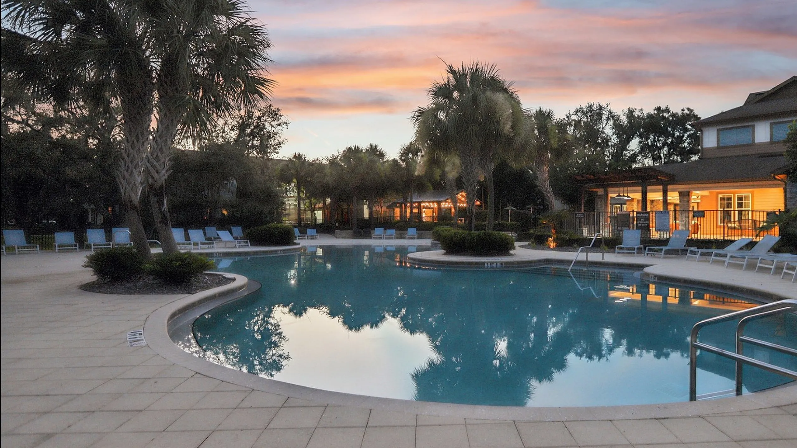 Inviting poolside paradise with palm trees and relaxing lounge chairs, set against a stunning sunset backdrop.