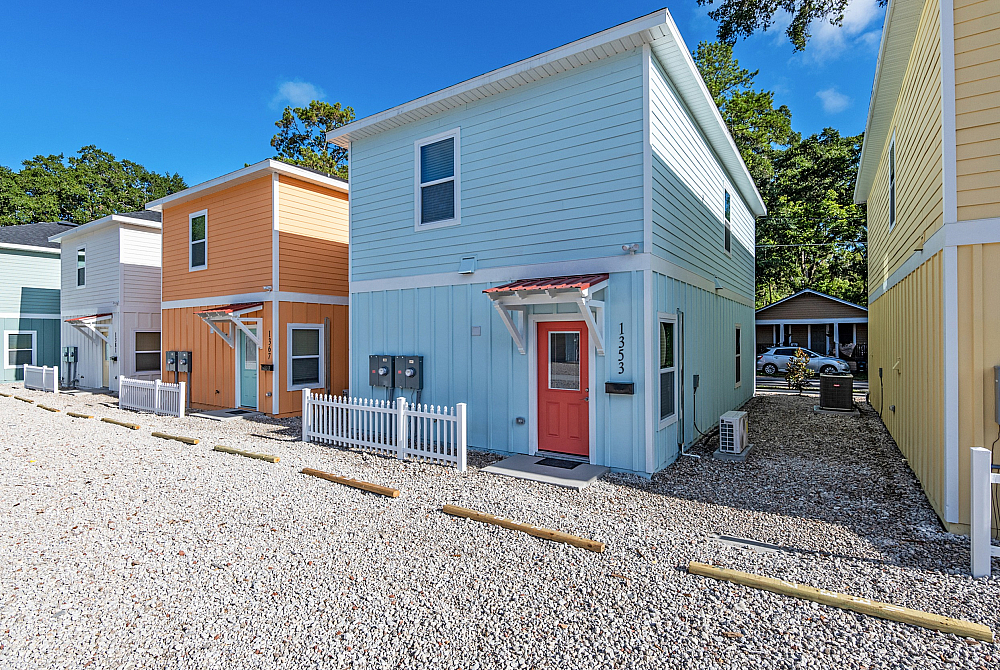 Charming row of colorful two-story homes with welcoming front porches, surrounded by vibrant greenery and a bright blue sky.