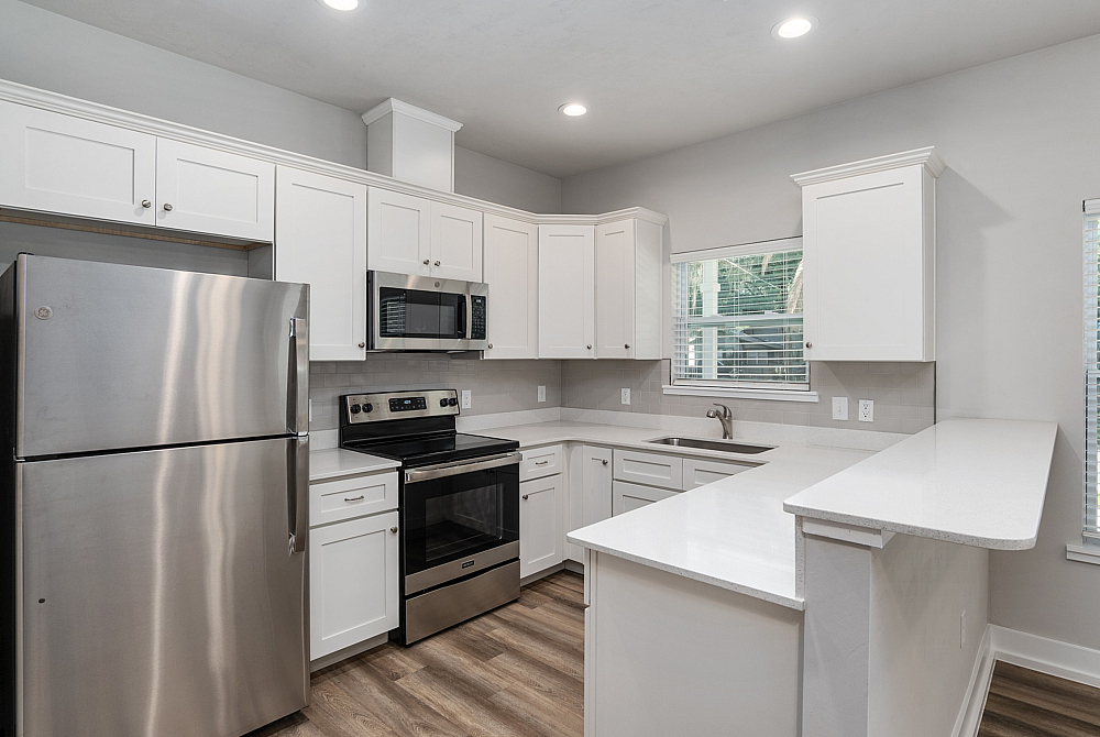 Modern kitchen with sleek stainless steel appliances, pristine white cabinets, and elegant wood flooring.