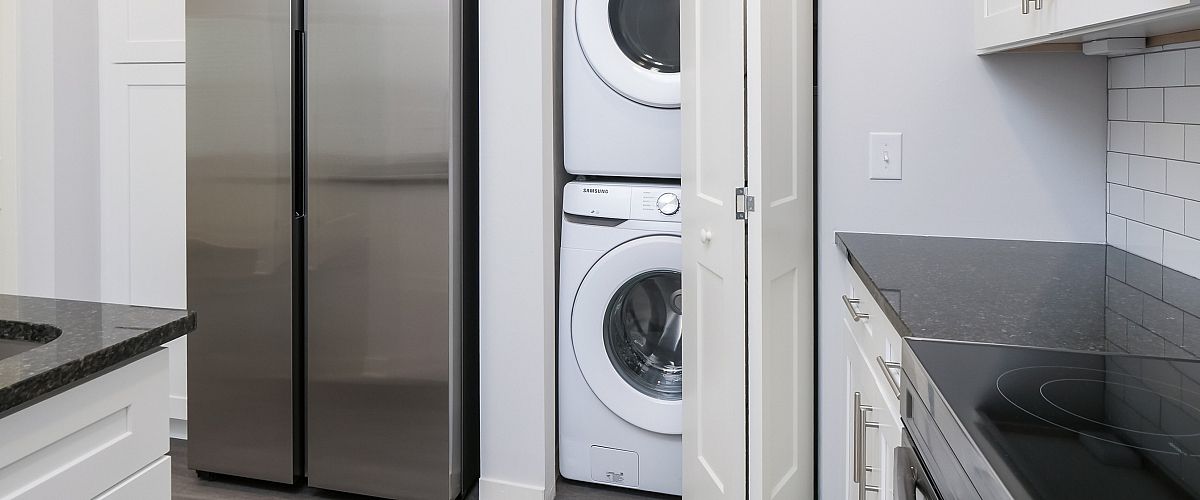 Modern kitchen space featuring sleek stainless steel appliances, pristine white cabinetry, and a convenient in-unit laundry area.
