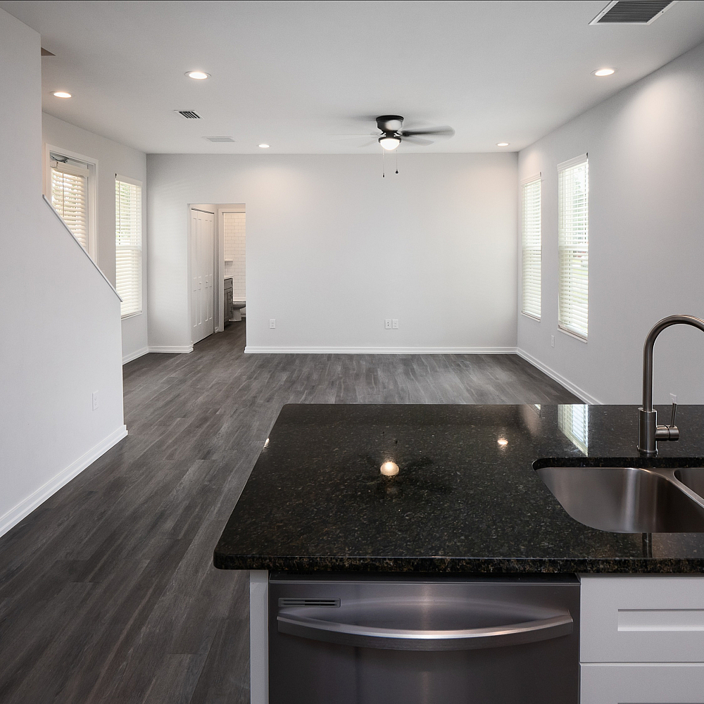 Modern open-concept living area with sleek hardwood floors, bright natural light, and a polished kitchen island featuring a double sink.