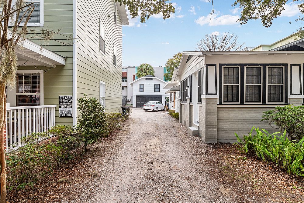 Charming neighborhood view with quaint homes, lush greenery, and a peaceful gravel path leading to a cozy garage.