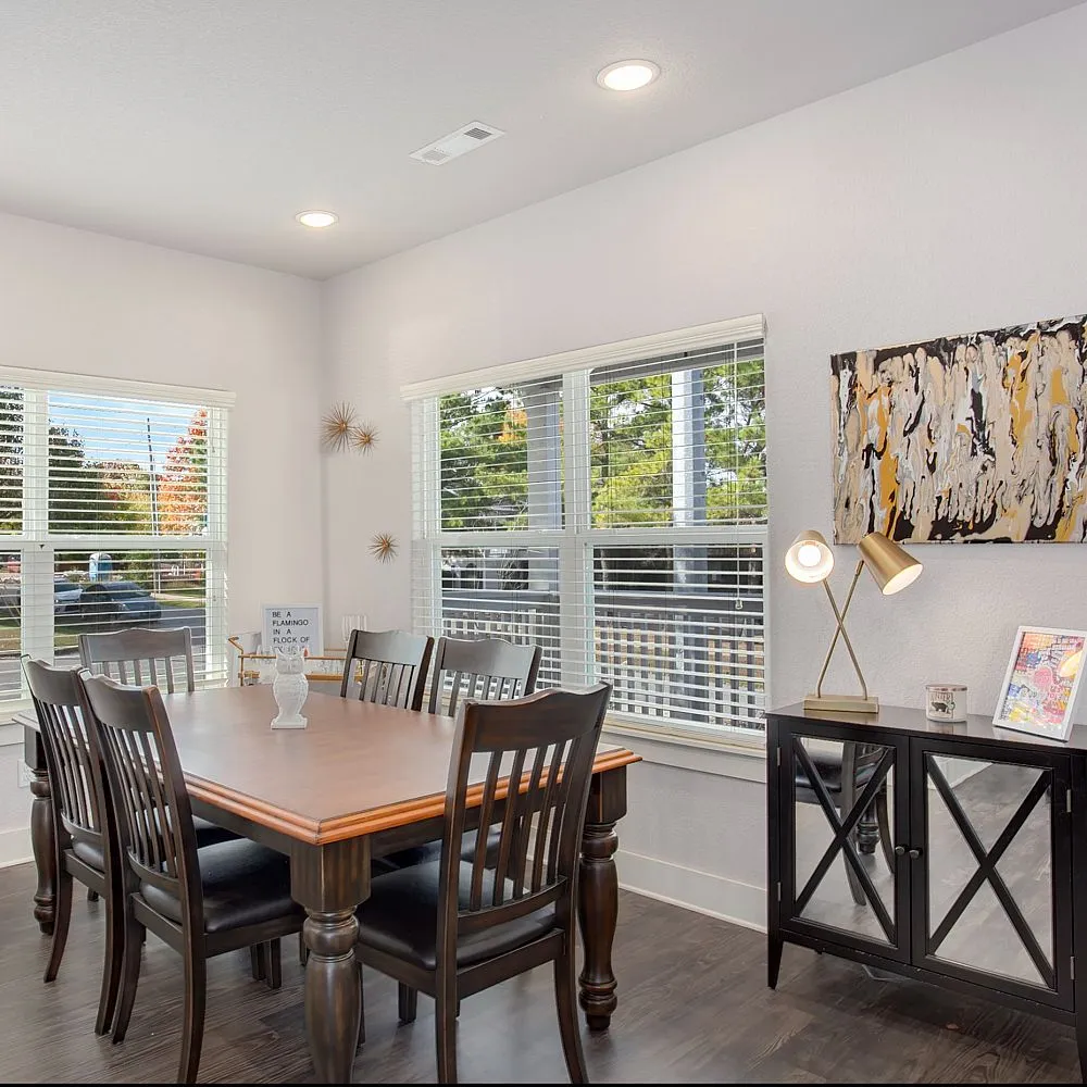 Bright dining area with modern art, sleek wooden table, and stylish chairs, enhanced by large windows with picturesque views.