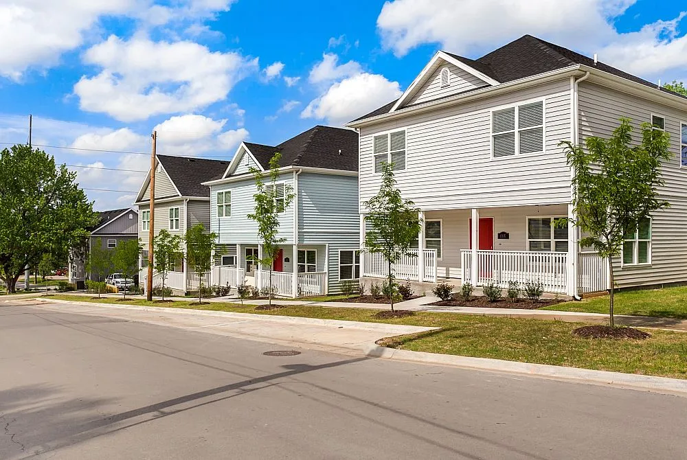 Charming suburban street lined with modern two-story homes featuring inviting front porches and vibrant red doors under a clear blue sky.