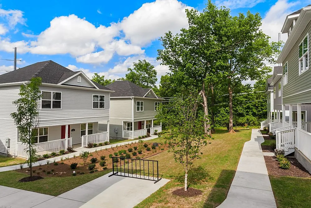 Charming residential neighborhood featuring modern two-story townhouses, lush green surroundings, and serene walkways on a sunny day.