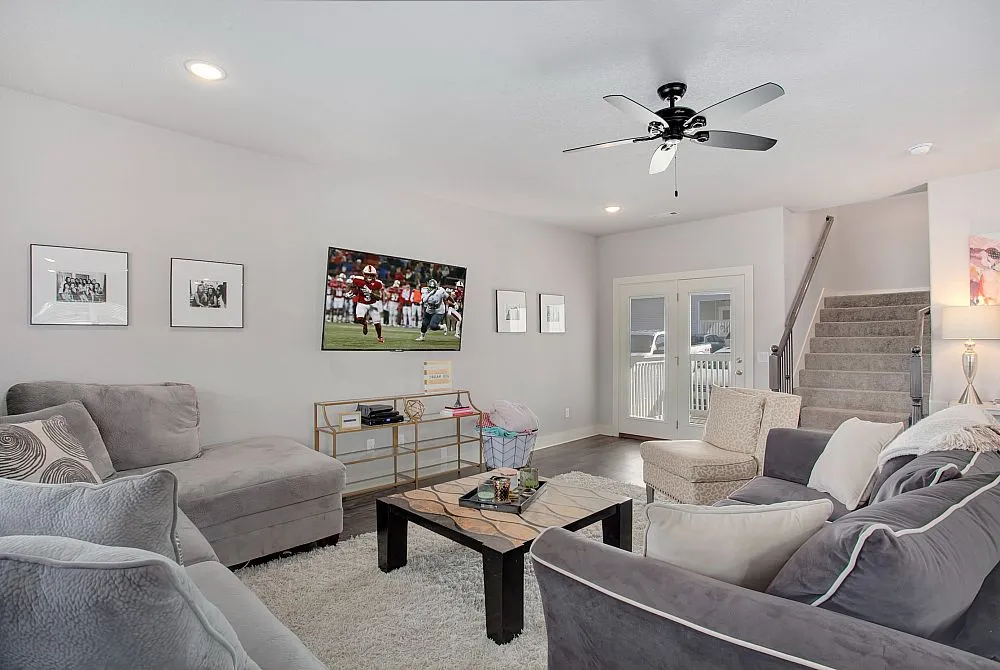 Inviting living room with plush sofas, modern decor, flat-screen TV, and natural light from large French doors.