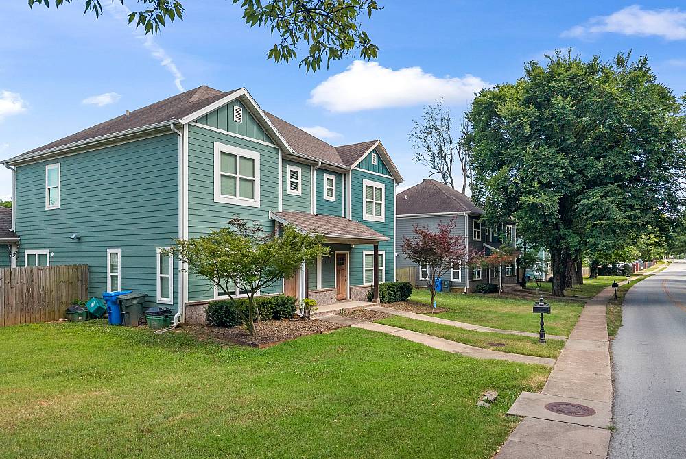 Charming suburban home with a green exterior, lush front lawn, and tree-lined street.