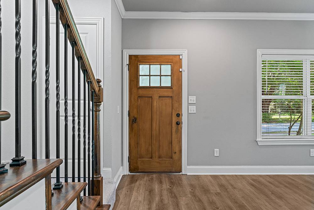 Charming entryway with elegant wood door, stylish staircase, and large window providing natural light.