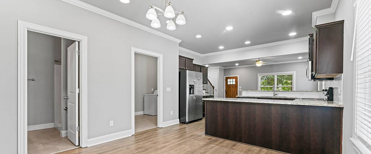 Elegant open-plan kitchen area featuring modern lighting, sleek dark cabinetry, and polished wood flooring.