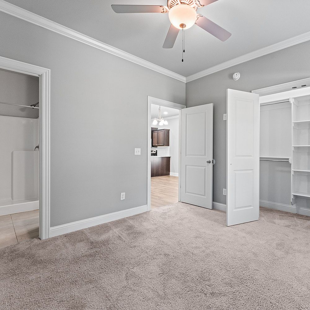 Bright bedroom with plush carpet, open closet, and view into a modern kitchen, perfect for cozy living.