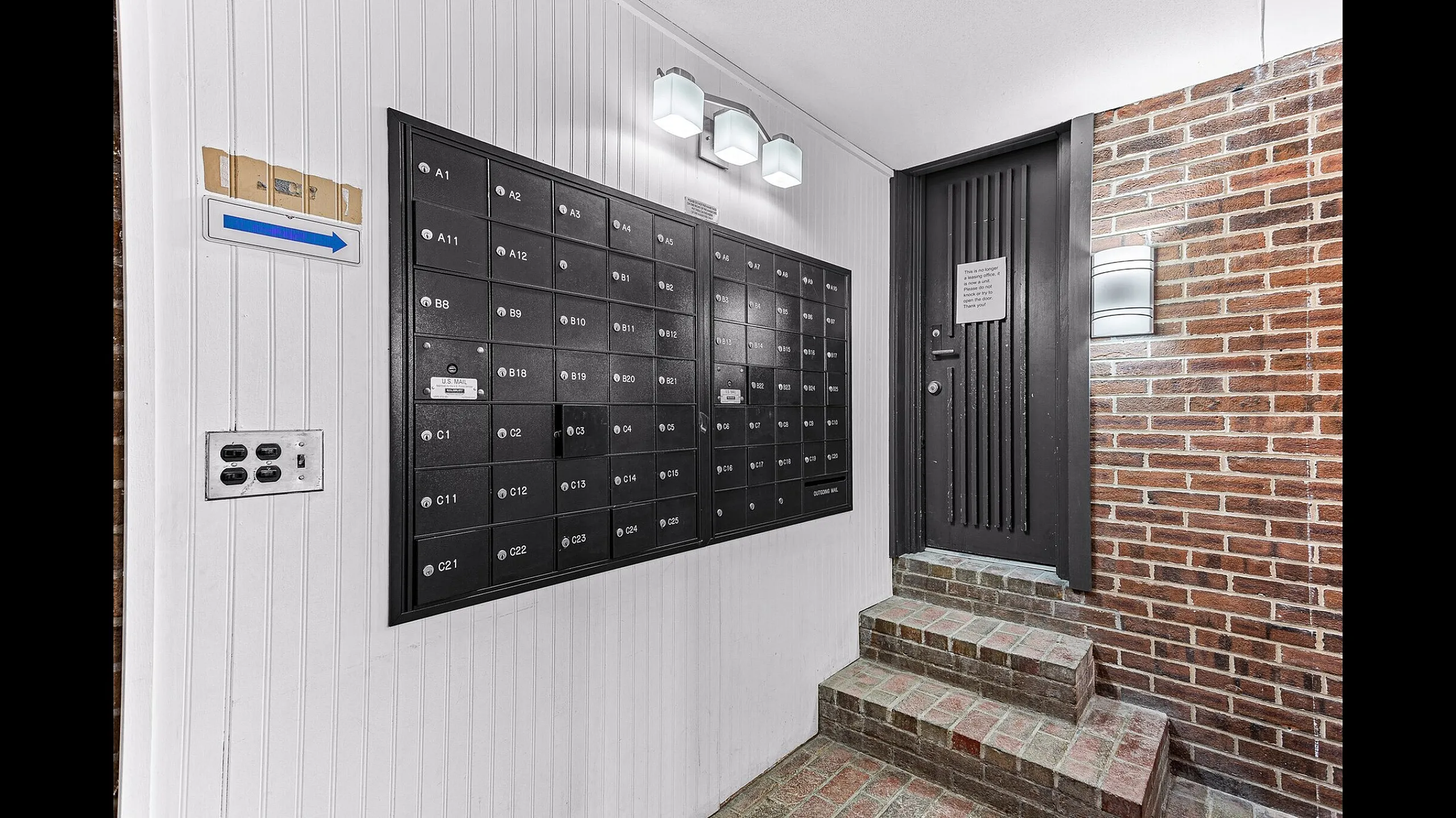 Chic apartment lobby area featuring modern black mailboxes on a stylish white and brick wall with ambient lighting.