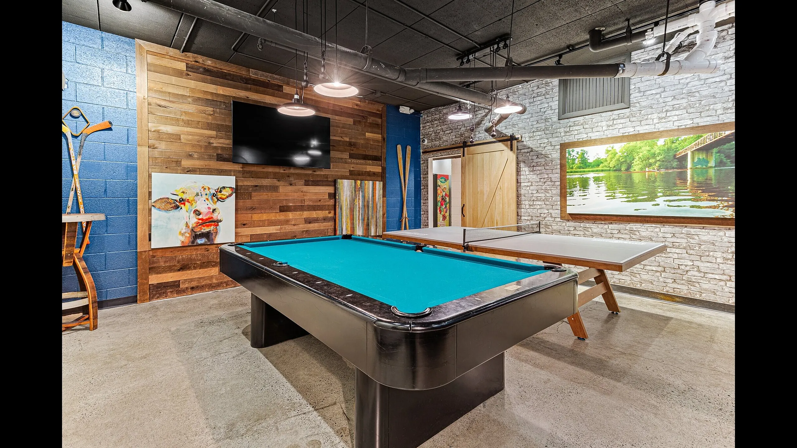 Chic entertainment room featuring a sleek pool table and ping pong setup, accented with vibrant artwork and rustic wood paneling.