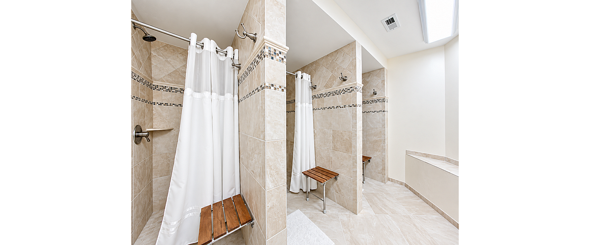 Elegant tiled shower area featuring dual stalls with modern fixtures and wooden seating, providing a luxurious spa-like experience.
