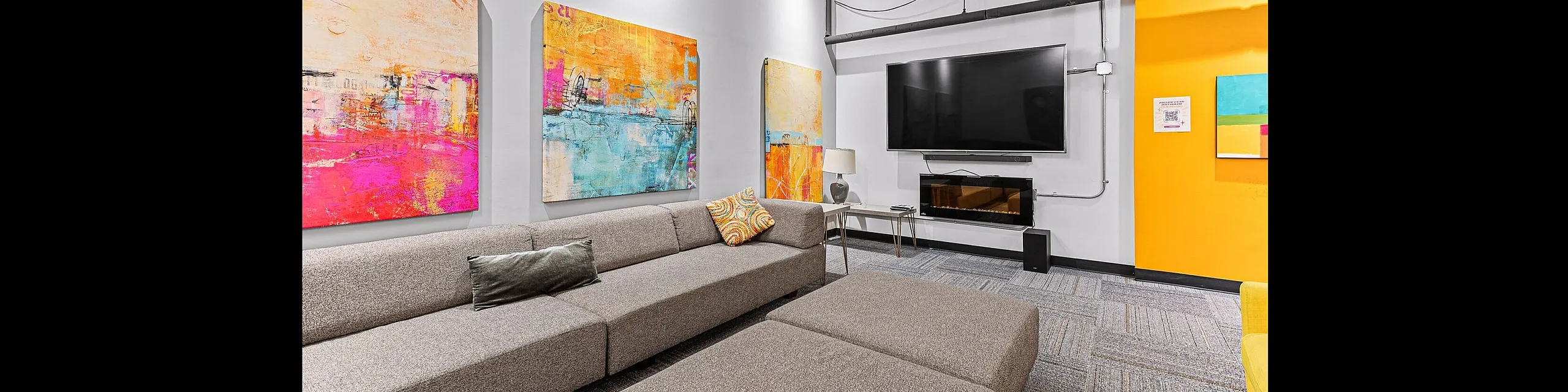 Chic living room with modern gray sectional sofa, vibrant abstract artwork, and sleek wall-mounted TV, perfect for relaxation and entertainment.