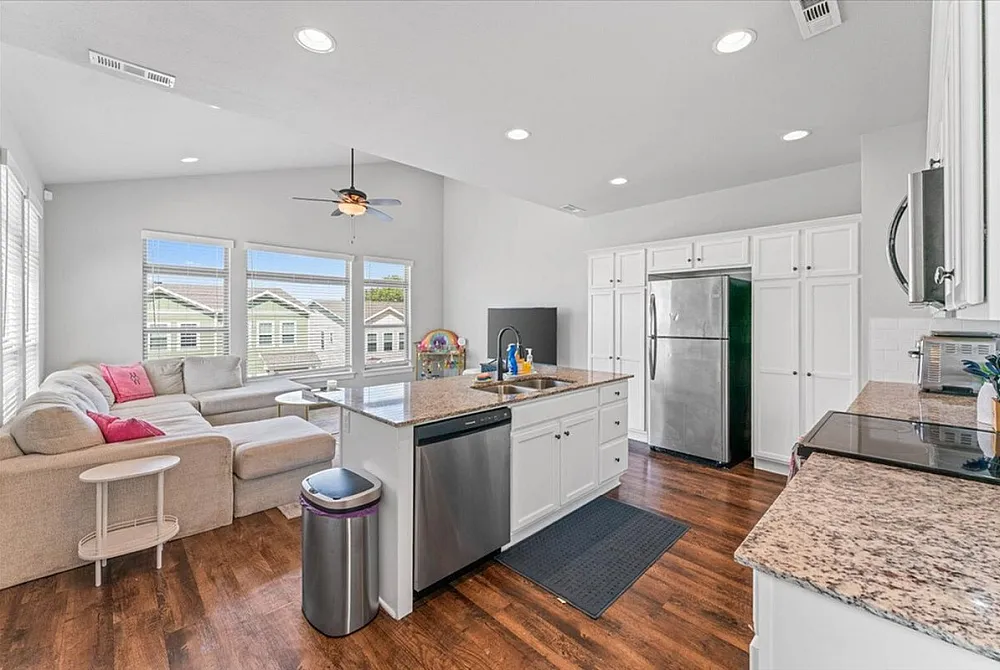 Beautiful open-concept kitchen and living area featuring modern appliances, granite countertops, and cozy sectional sofa bathed in natural light.