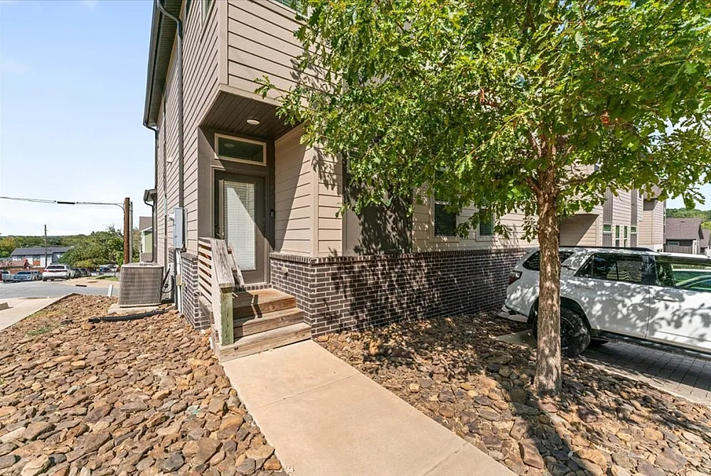 Charming townhouse entrance with a modern facade, surrounded by lush greenery and a neatly paved driveway.